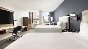 A hotel room with two beds, a desk, a chair, a TV, and a window with a city view.
