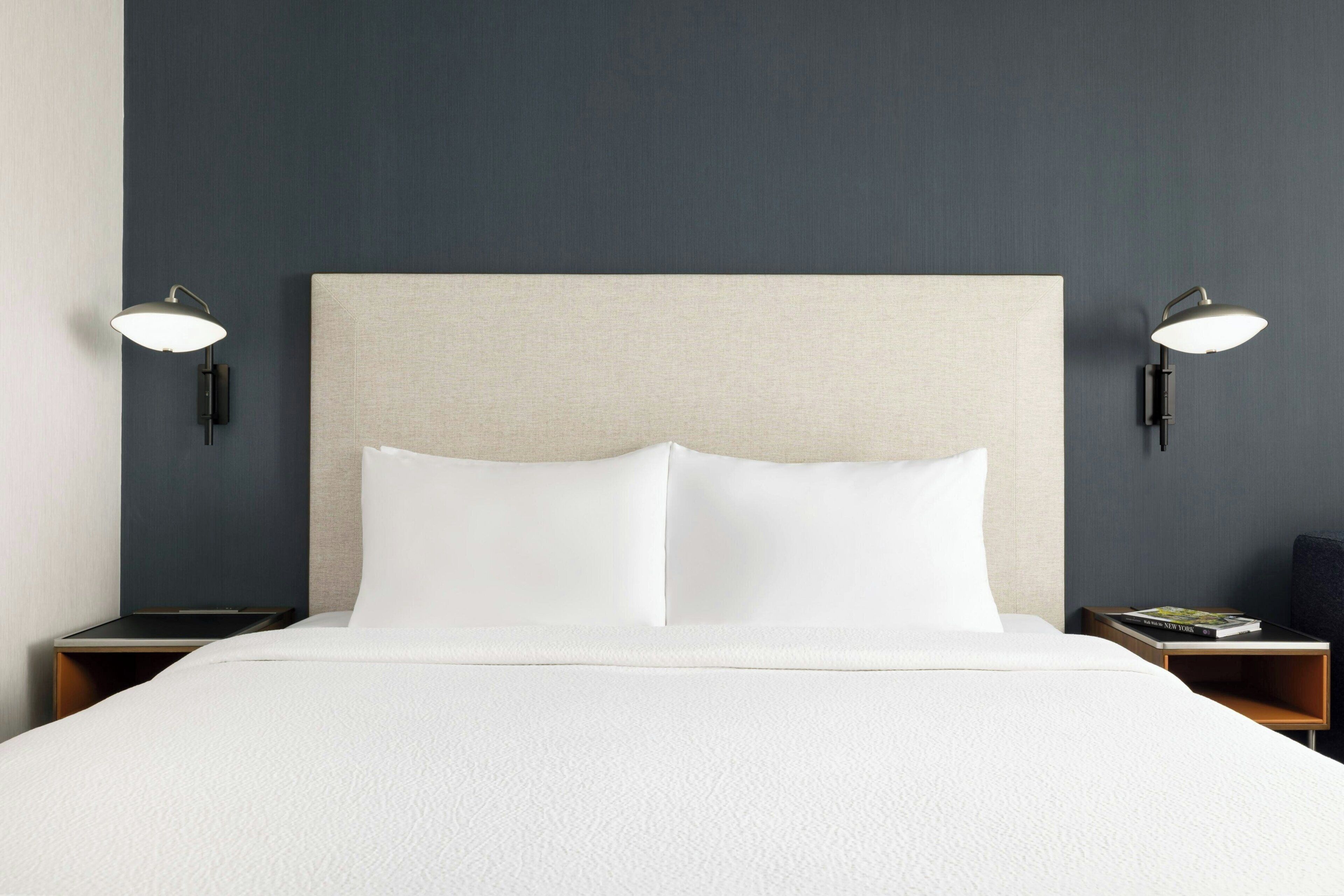 Quarto de hotel com uma cama grande, duas mesas de cabeceira e luminárias fixadas na parede.