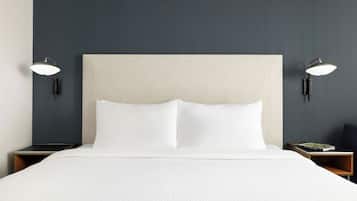 Quarto de hotel com uma cama grande, duas mesas de cabeceira e luminárias fixadas na parede.