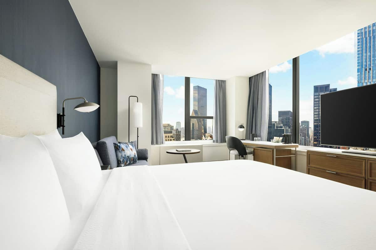 Quarto de hotel com cama grande, escrivaninha, cadeira, televisão e vista para a cidade.