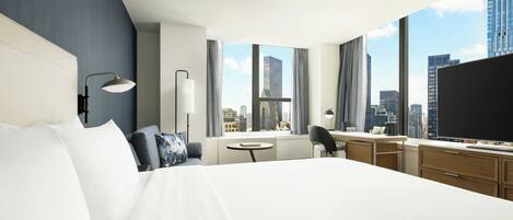 Habitación de hotel con una cama grande, un escritorio, una silla, un televisor y vistas a la ciudad.