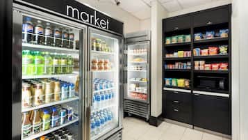 A refrigerated display case with beverages and snacks, a microwave, and shelves with packaged goods.