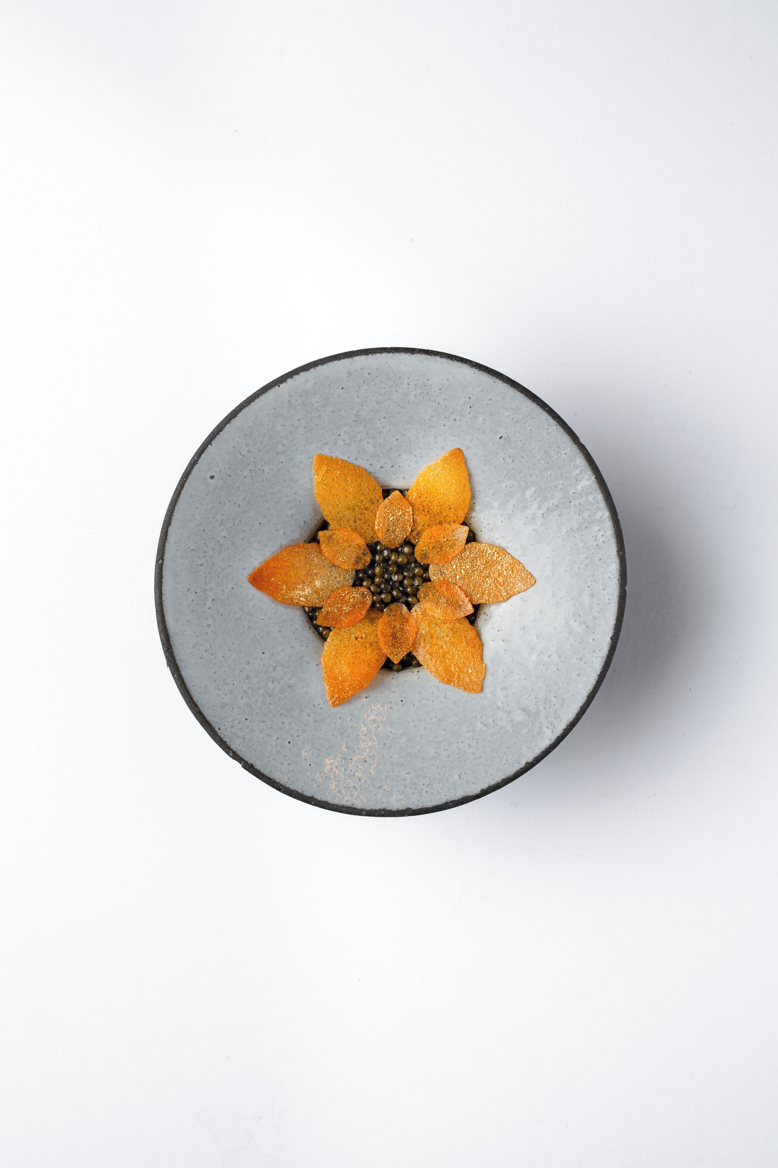 A round ceramic plate with a flower-like arrangement of orange slices and black seeds on a white background.