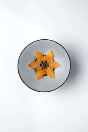 A round ceramic plate with a flower-like arrangement of orange slices and black seeds on a white background. - Martinique New York on Broadway, Curio Collection by Hilton (New York)