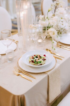 A table set for a formal dining occasion with clear glassware, gold cutlery, and a white plate with a salad. - Martinique New York on Broadway, Curio Collection by Hilton (New York)