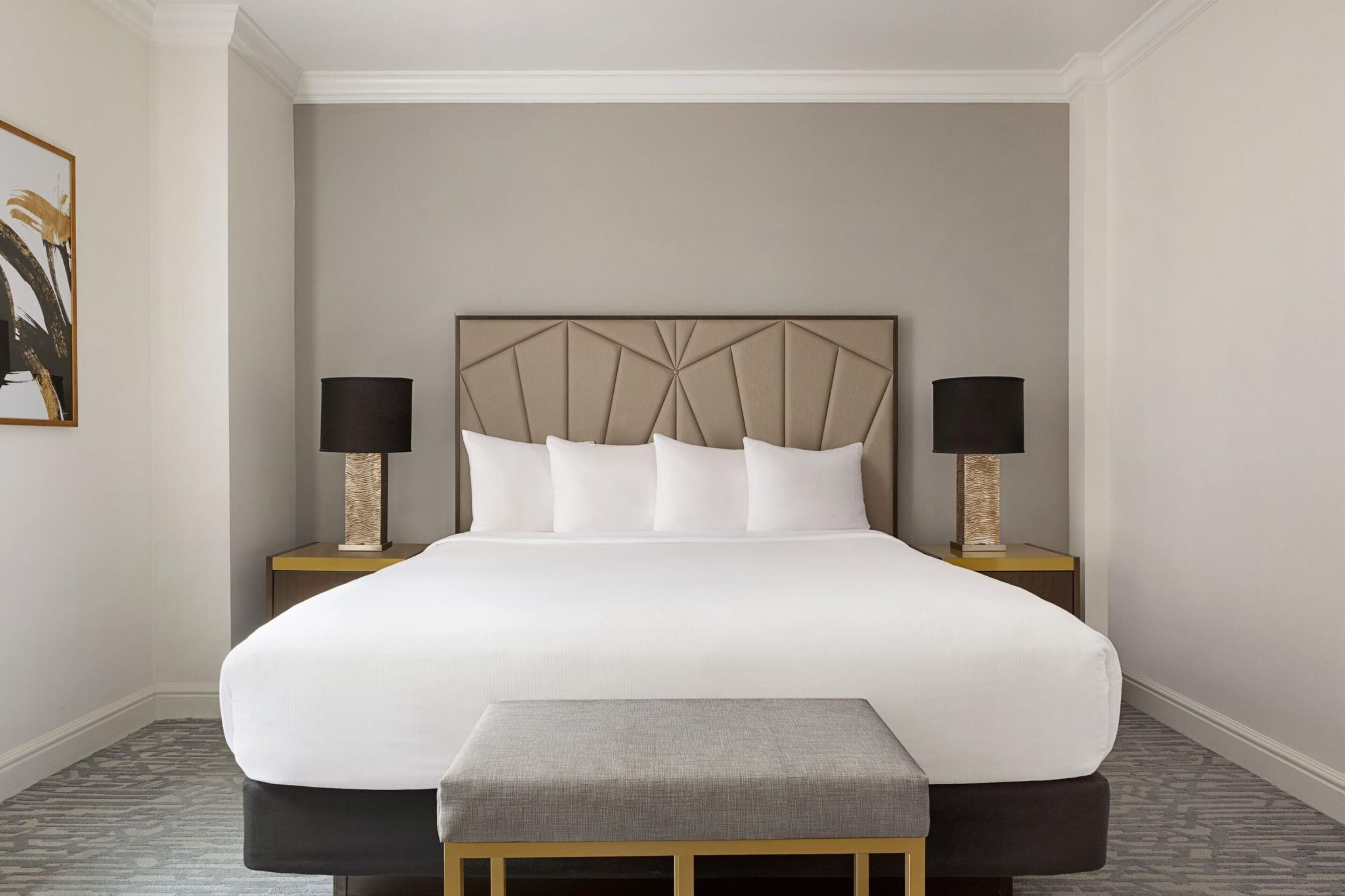 A neatly made bed with a headboard, two bedside tables with lamps, and a bench at the foot of the bed.