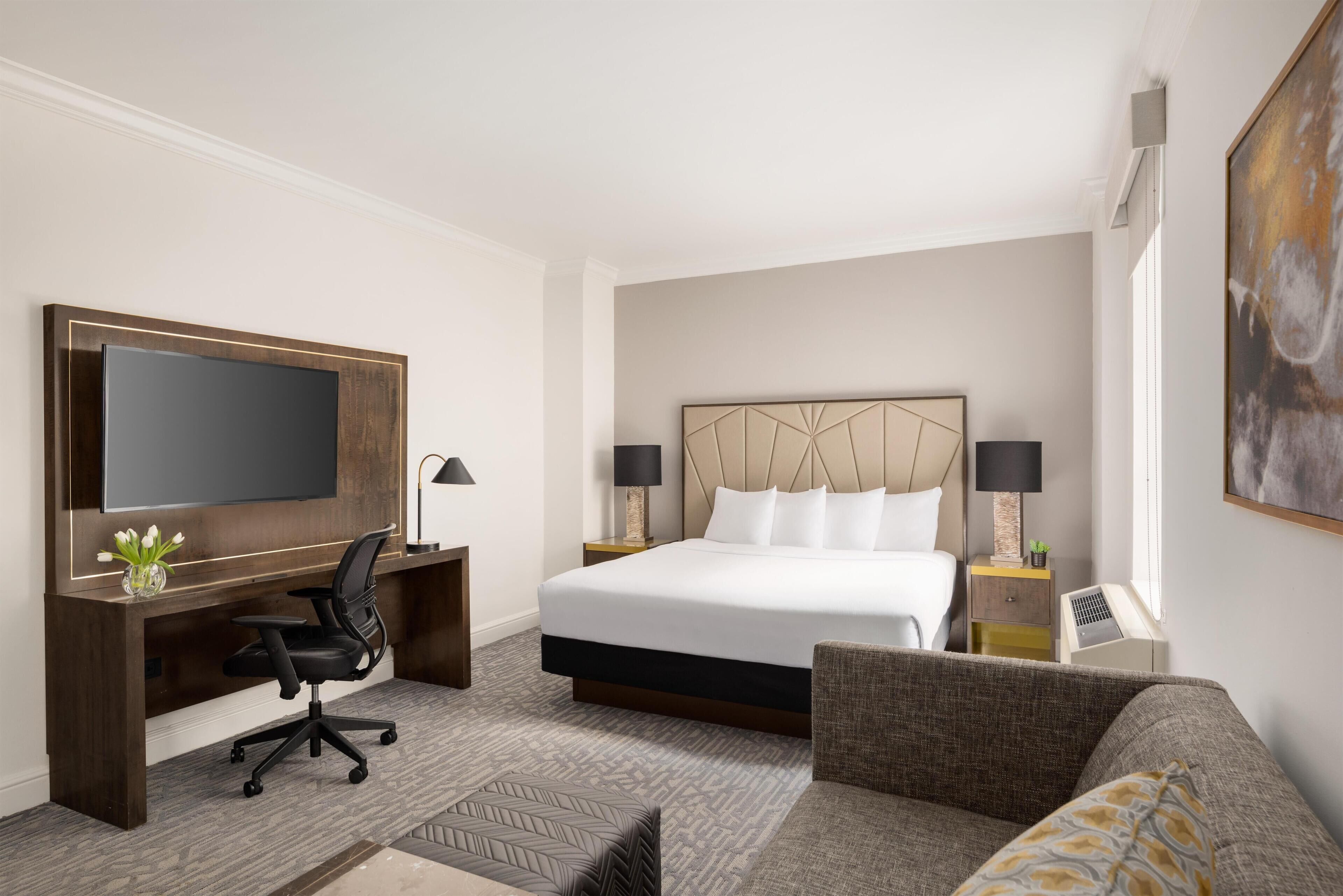 Ein Hotelzimmer mit einem großen Bett, einem Schreibtisch mit Stuhl, einem Fernseher und einer Couch.