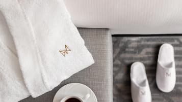 A white towel with a gold embroidered star, a cup of coffee, and a pair of white slippers on a grey textured surface.