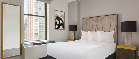 A hotel room with a large bed, two bedside tables, a window with a view of buildings, and a radiator.