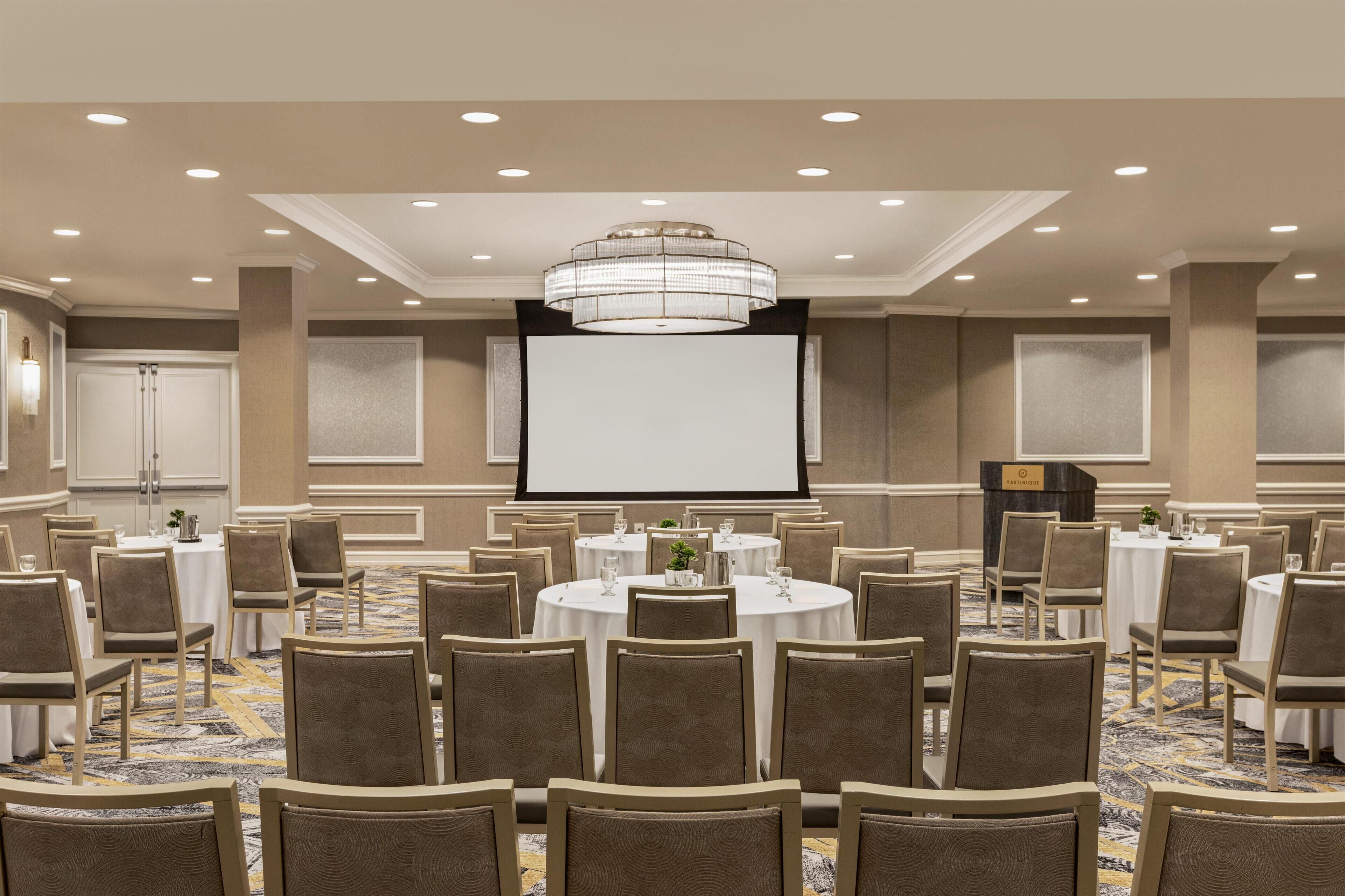 A conference room with round tables, chairs, a projector screen, and a chandelier.