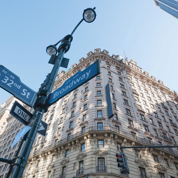 Señal de calle que indica Broadway y la 32 Calle, un edificio alto de arquitectura clásica, y un semáforo.