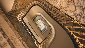 Una escalera de mármol con ornamentales barandillas doradas y un espejo circular en la parte superior.
