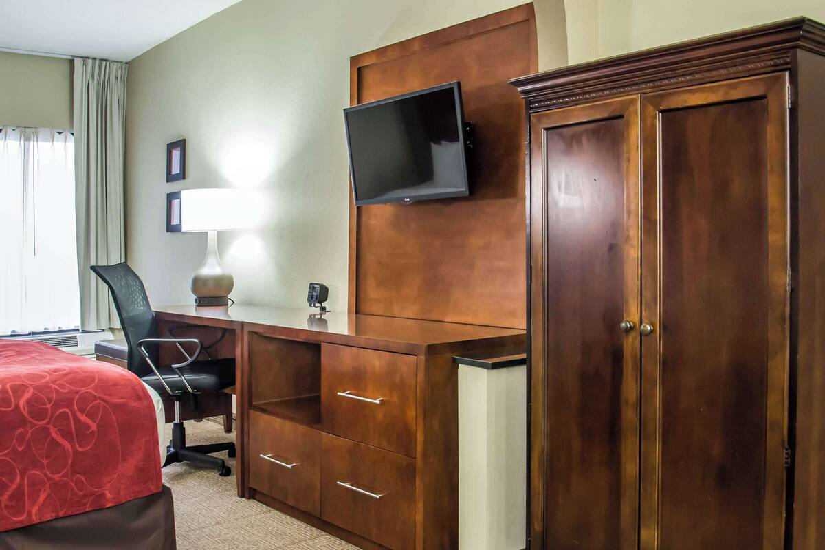 Une chambre d’hôtel comprenant un lit, un bureau avec une chaise, un téléviseur fixé au mur et une grande armoire en bois.