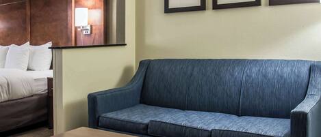 A hotel room with a blue sofa, a wooden coffee table, and a bed with white linens. There are three framed pictures on the wall.