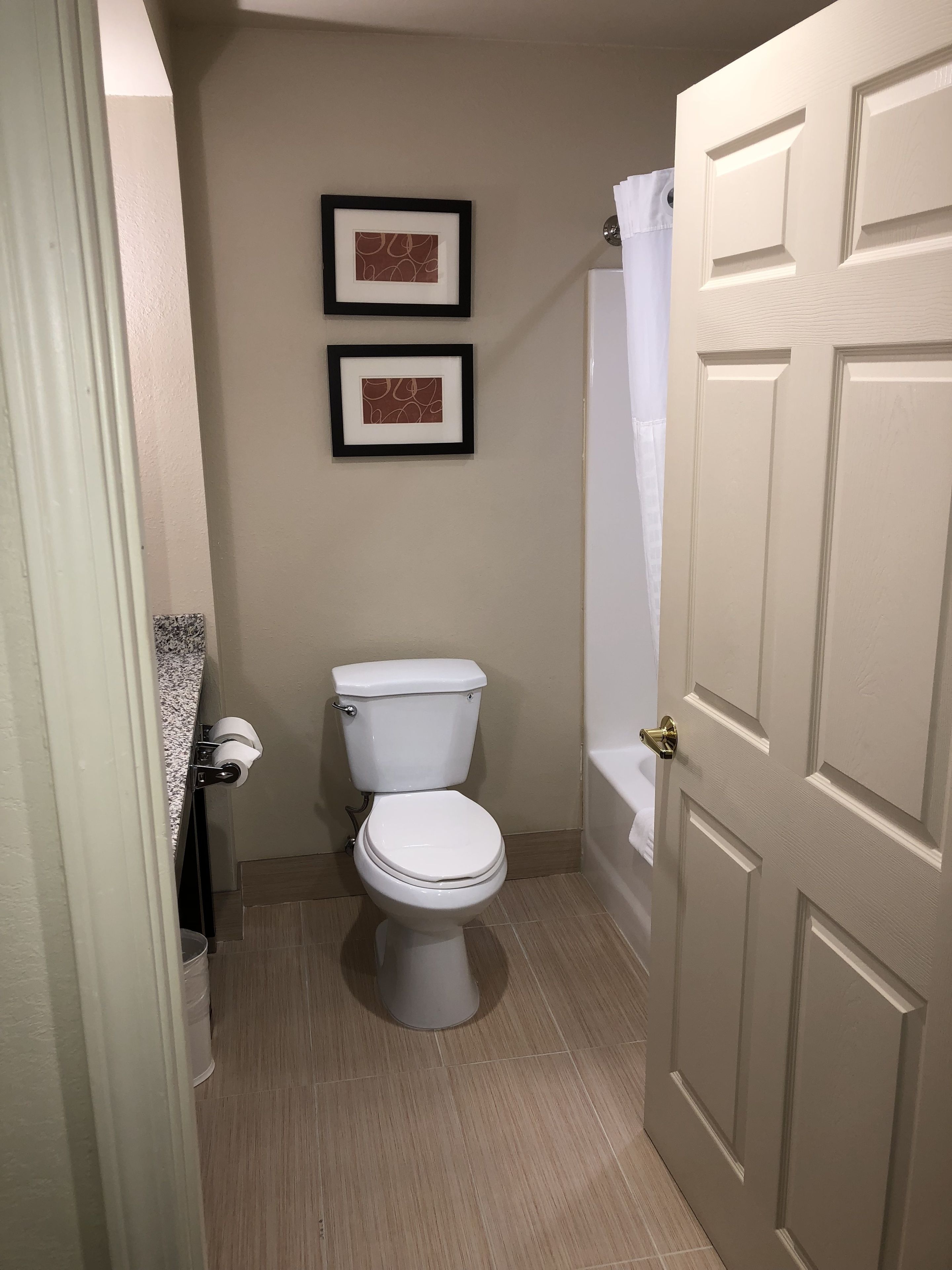 A small, clean bathroom with a toilet, two framed pictures on the wall, and a shower curtain.