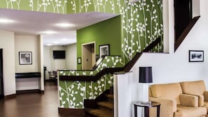 A hotel lobby with a green and white patterned wall, a staircase, a reception desk, a sofa, and a small table.