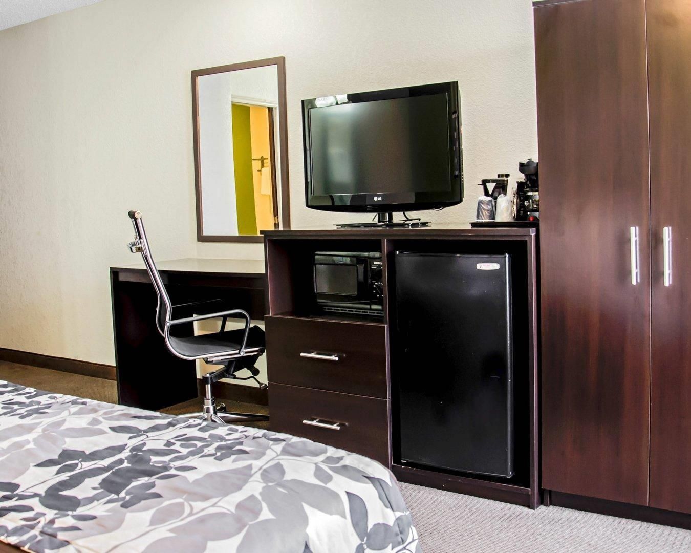 Una habitación de hotel con cama, escritorio con silla, televisor, refrigerador y armario.