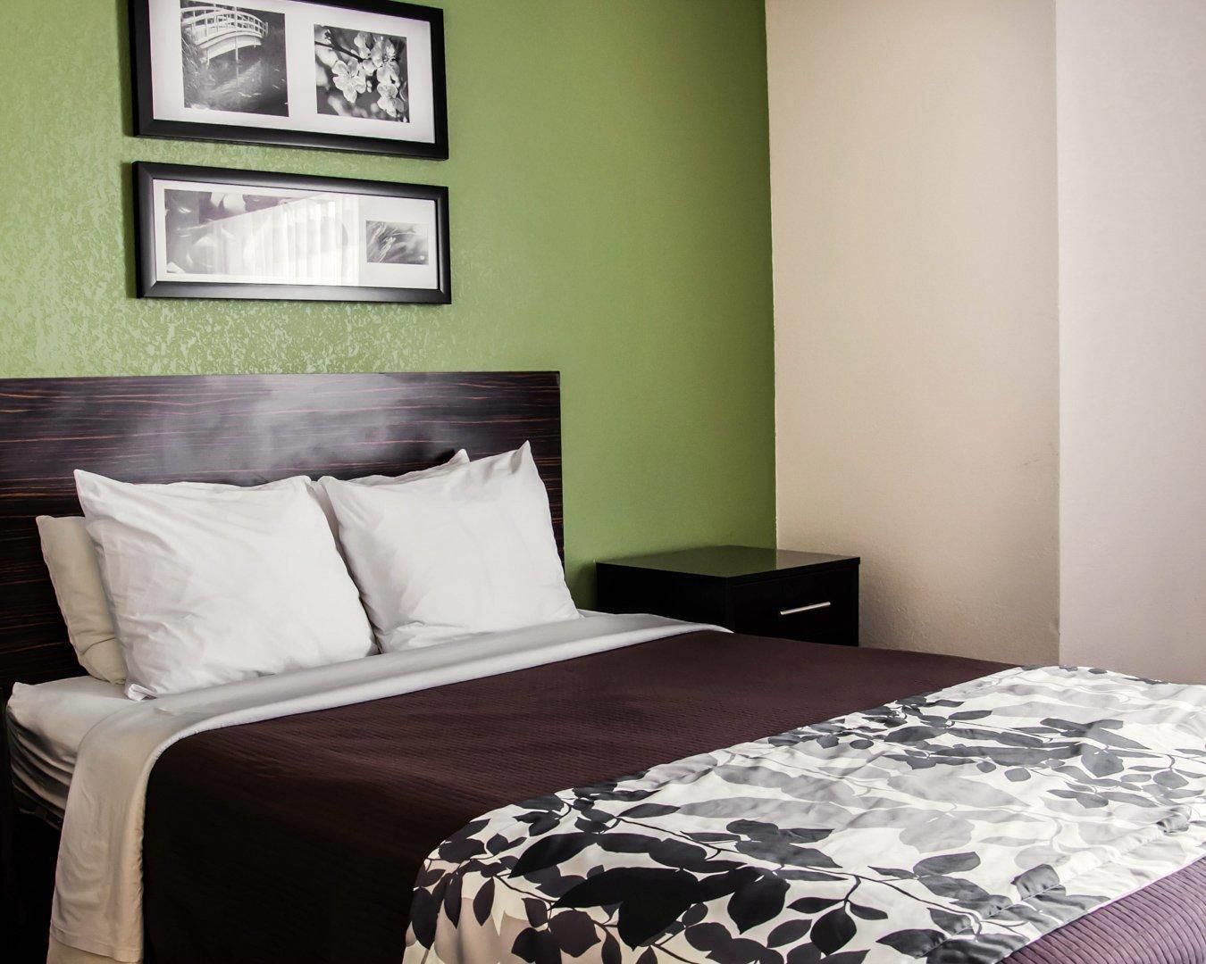 A neatly made bed with white linens and a floral-patterned blanket, a dark wooden headboard, and two framed pictures on the wall.