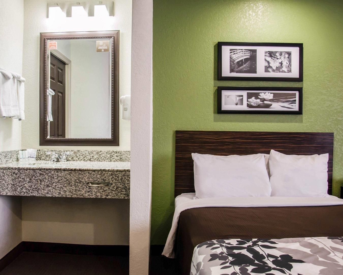 A hotel room with a granite countertop sink, a mirror, a bed with white bedding, and two framed pictures on the wall.