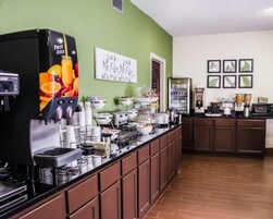 Un bar de desayuno autoservicio con dispensador de zumos de frutas, máquinas de café y una variedad de alimentos.
