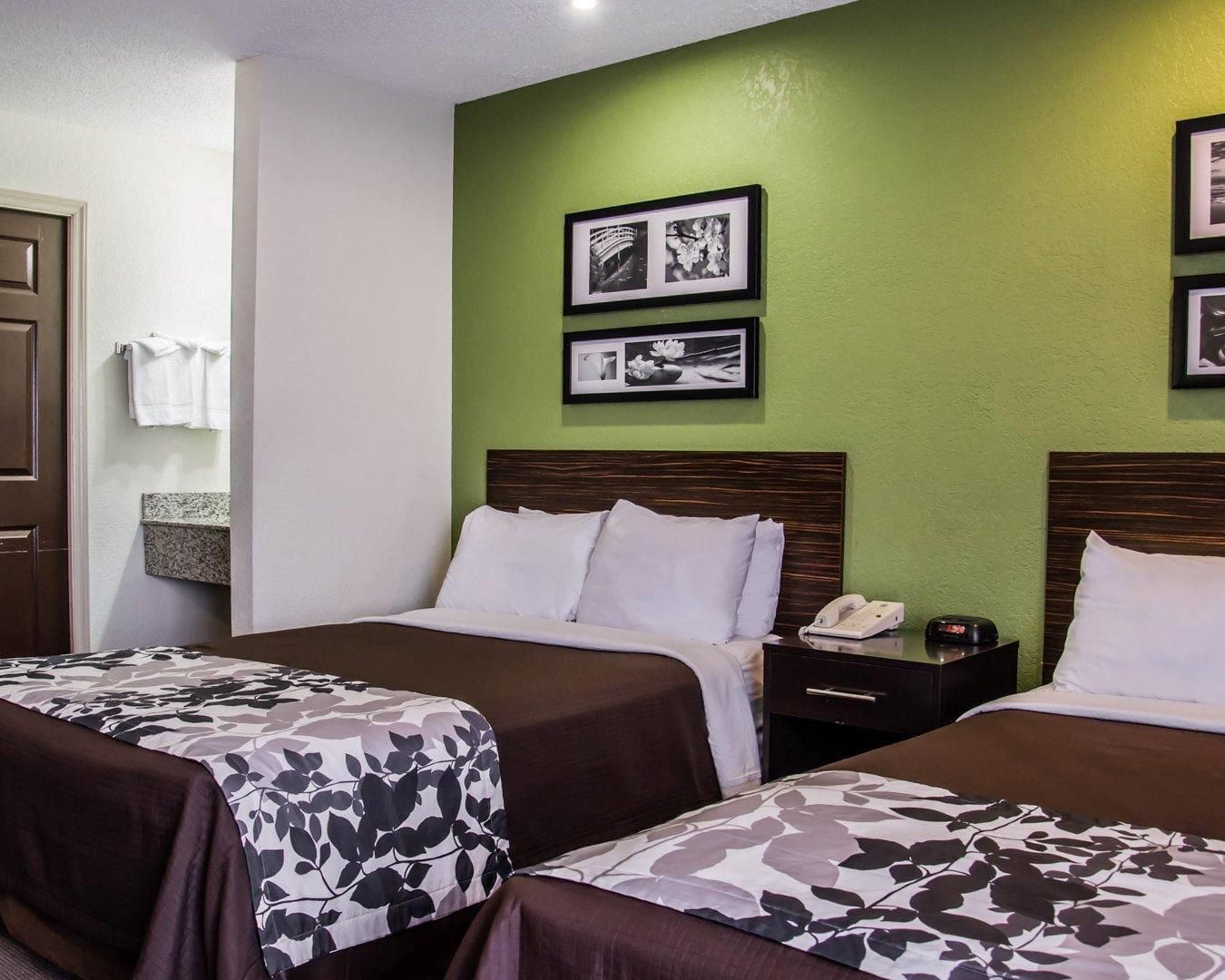 A hotel room with two beds, a bedside table with a phone, and a wall with framed pictures.
