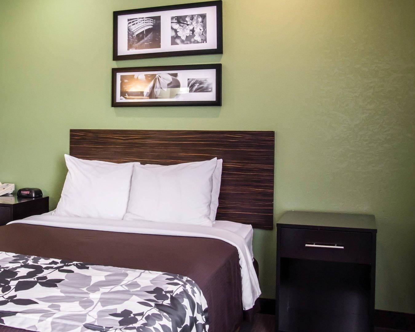Una habitación de hotel con una cama, una mesita de noche, un cajón y dos cuadros en la pared.