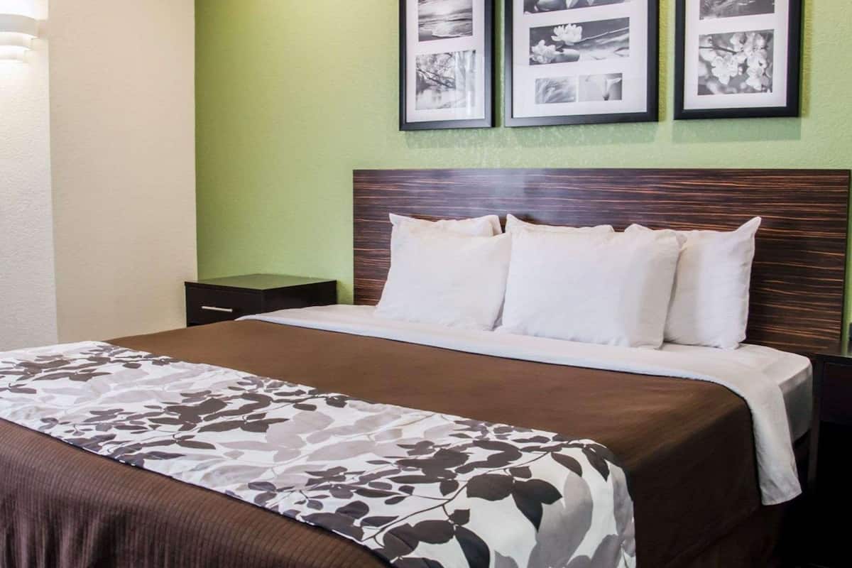 A neatly made bed with a brown and white floral bedspread, a wooden headboard, and a green wall with three framed pictures above it.