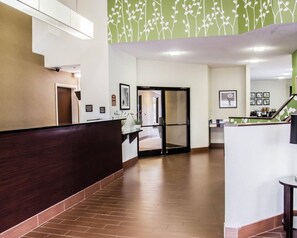 A reception area with a dark wooden reception desk, a glass door entrance, and a green wall with white floral patterns.