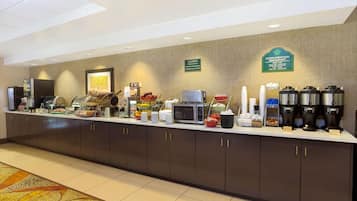 A breakfast bar with a variety of food items, a coffee station, and a caution sign.