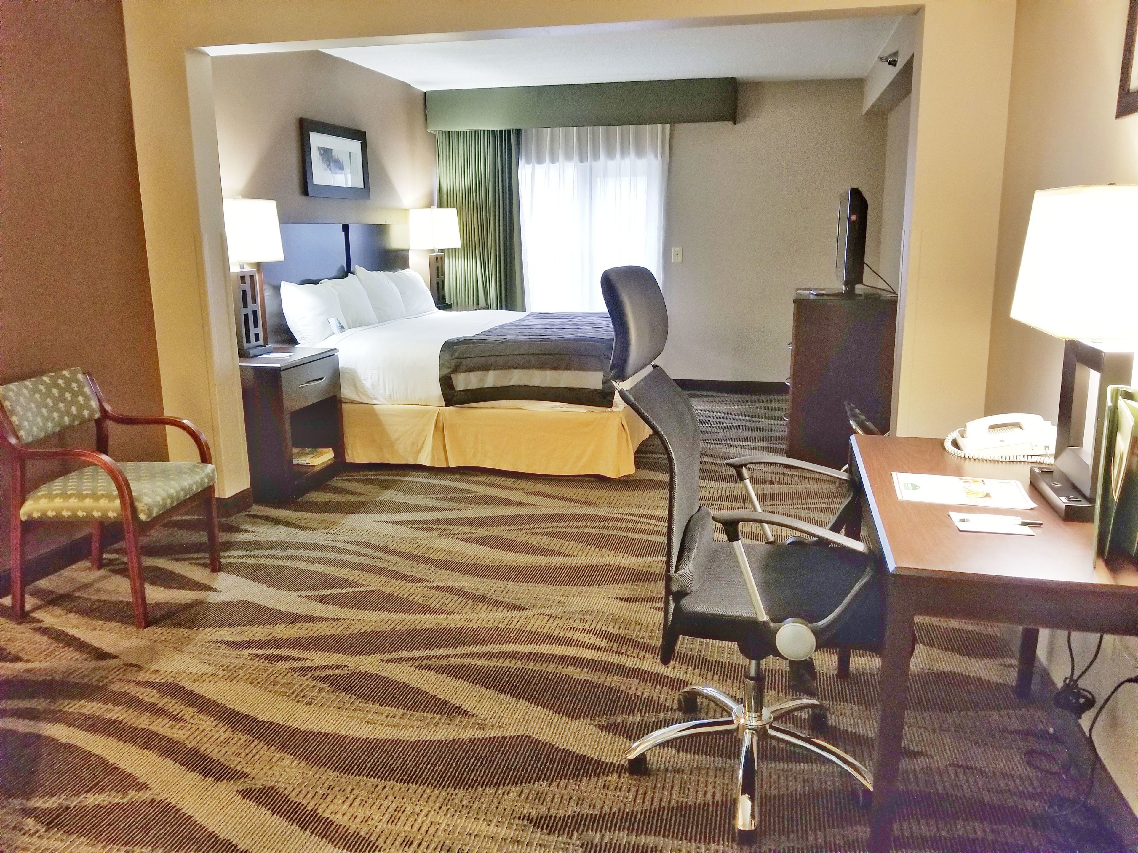 A hotel room with a bed, two chairs, a desk, and a telephone.