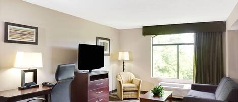 Habitación de hotel con escritorio, televisor, silla, sofá y ventana con cortinas.