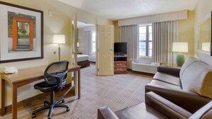 A hotel room with a desk, chair, couch, TV, and a framed picture on the wall. - Extended Stay America Suites - Fayetteville - Fort Bragg (Fayetteville)