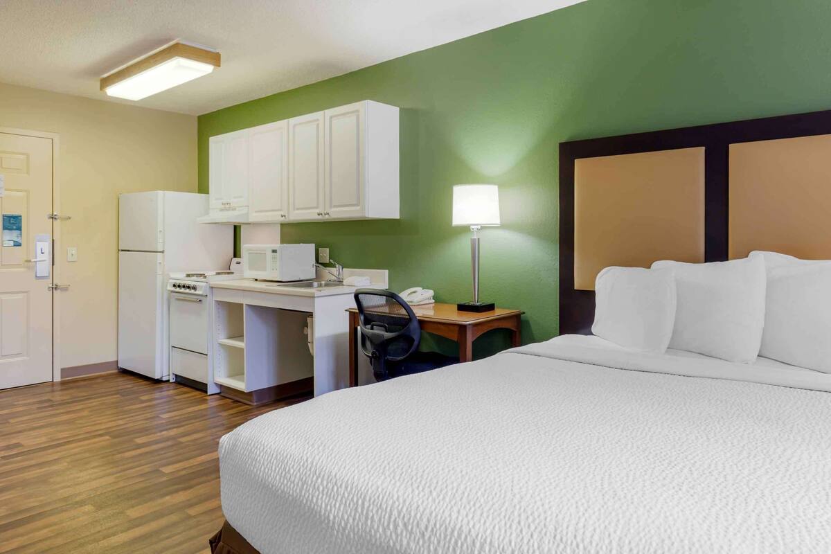 A hotel room with a bed, a desk with a microwave, a refrigerator, and a chair.