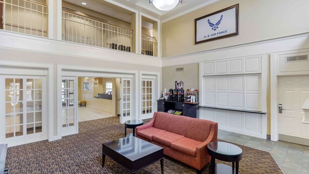 A spacious lobby with a high ceiling, a red sofa, a coffee station, and a U.S. Air Force emblem on the wall. - Extended Stay America Suites - Fayetteville - Fort Bragg (Fayetteville)