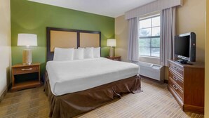 A hotel room with a large bed, two bedside tables with lamps, a television, and a window with curtains. - Extended Stay America Suites - Fayetteville - Fort Bragg (Fayetteville)