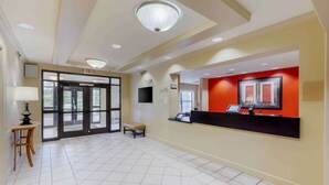 A hotel reception area with a reception desk, a bench, and an exit sign. - Extended Stay America Suites - Fayetteville - Fort Bragg (Fayetteville)