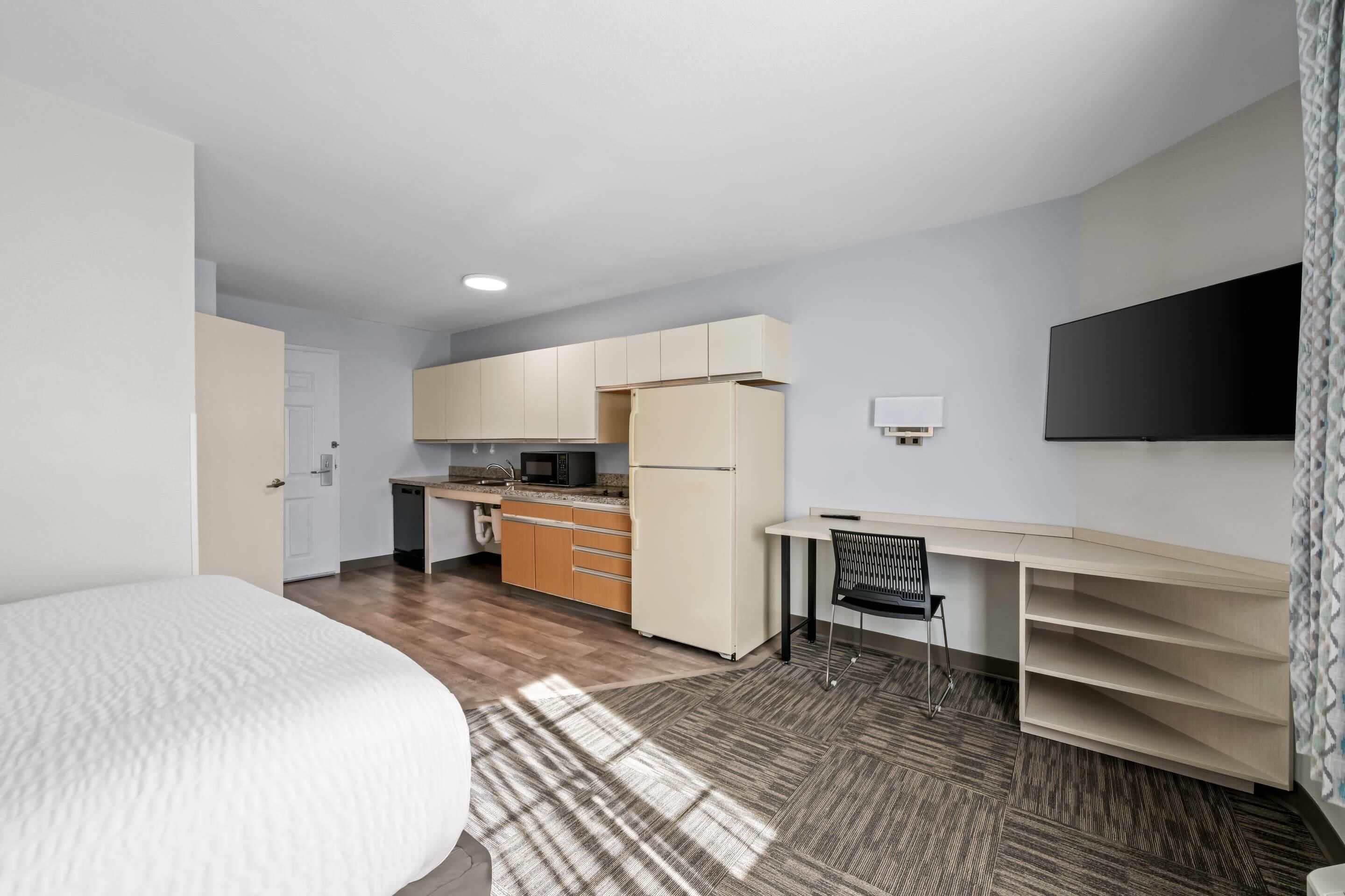 A compact room with a bed, a kitchenette, a TV, and a desk with a chair.