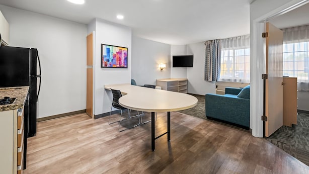 A modern kitchen with a refrigerator, a dining table, and a TV mounted on the wall. - MainStay Suites Greensboro (Greensboro)