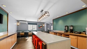 A modern kitchen with a long island, red bar stools, and a seating area with a bench and chairs. - MainStay Suites Greensboro (Greensboro)