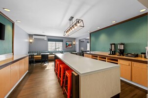 Una cocina moderna con una isla grande, taburetes rojos y una zona de estar con un banco y sillas.