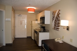 A compact kitchen with white appliances, a dining area with a table and chairs, and a hallway leading to a door. - MainStay Suites Greensboro (Greensboro)
