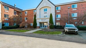 A MainStay Suites building with a brick facade, a central entrance, and a parking area with a white car. - MainStay Suites Greensboro (Greensboro)