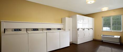 A laundry room with multiple washers and dryers, a large window, and a white air conditioning unit.