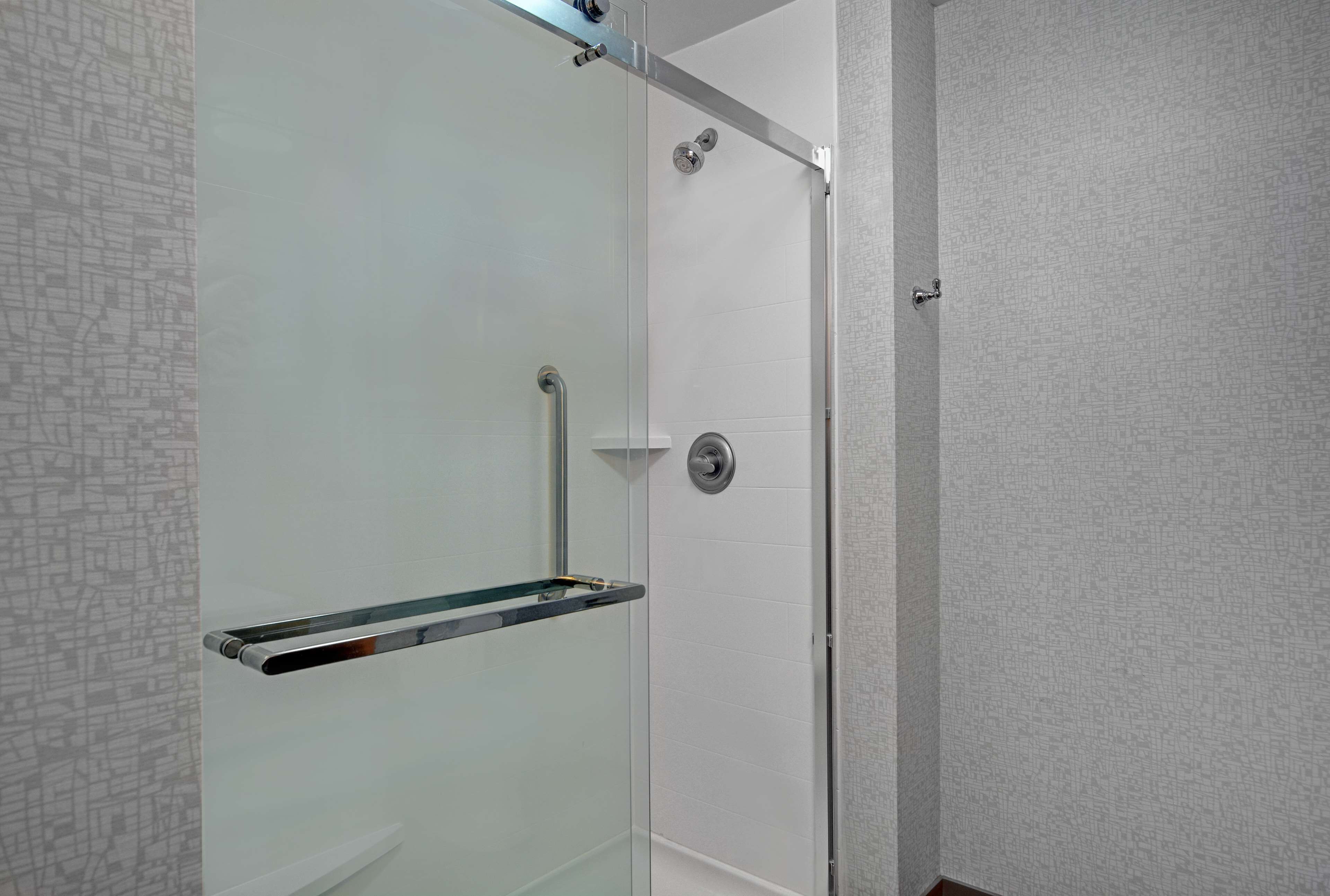 Una ducha moderna con puerta de cristal, grifo cromado y repisa de vidrio.