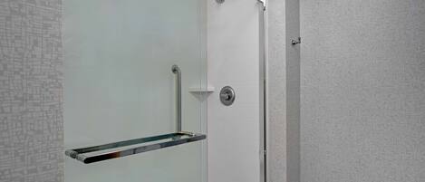 Una ducha moderna con puerta de cristal, grifo cromado y repisa de vidrio.