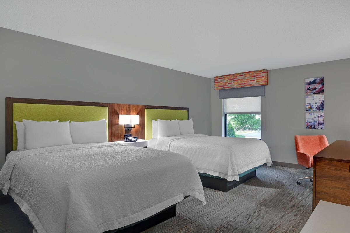 A hotel room with two beds, a desk, and a chair.