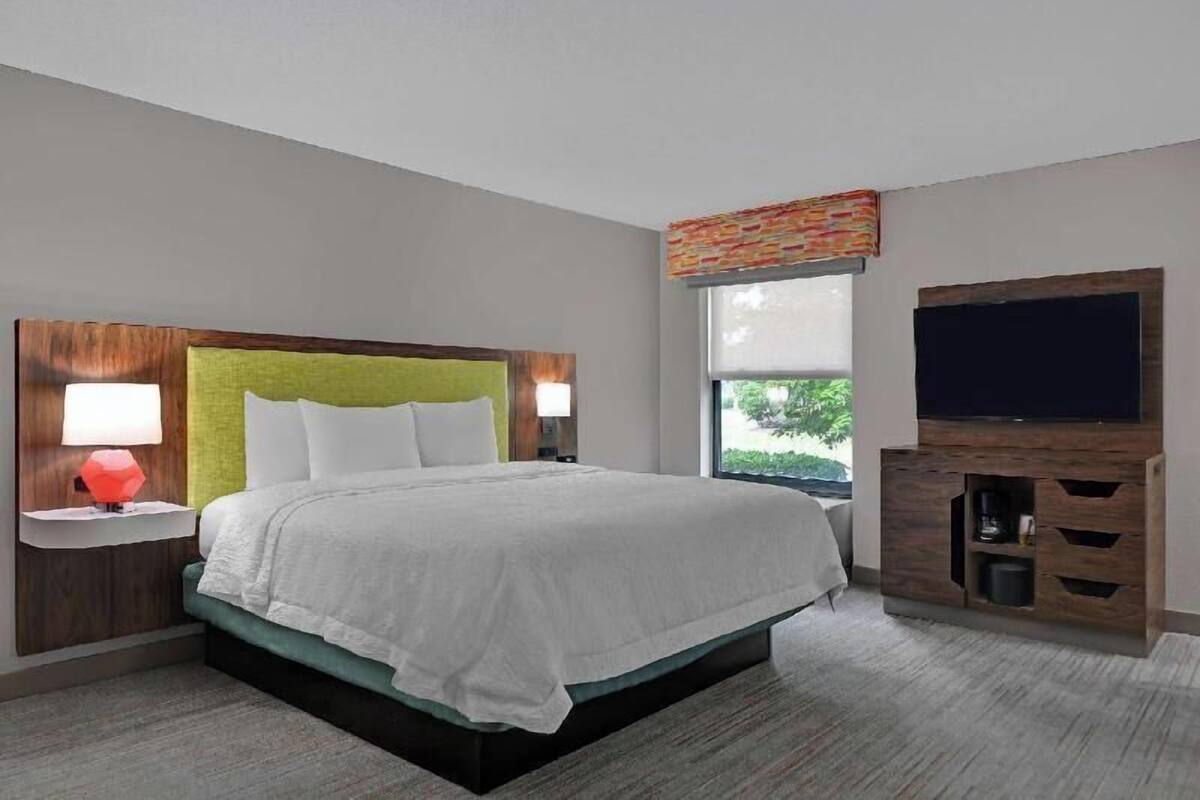 A modern hotel room with a bed, nightstands, a television, and a window with a view.