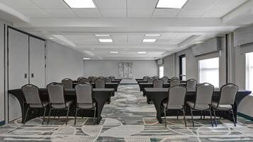 A conference room with rows of tables and chairs, a patterned carpet, and a large window on the right.