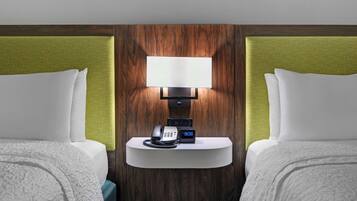 Habitación de hotel con dos camas, una mesita de noche con lámpara, teléfono y reloj digital.