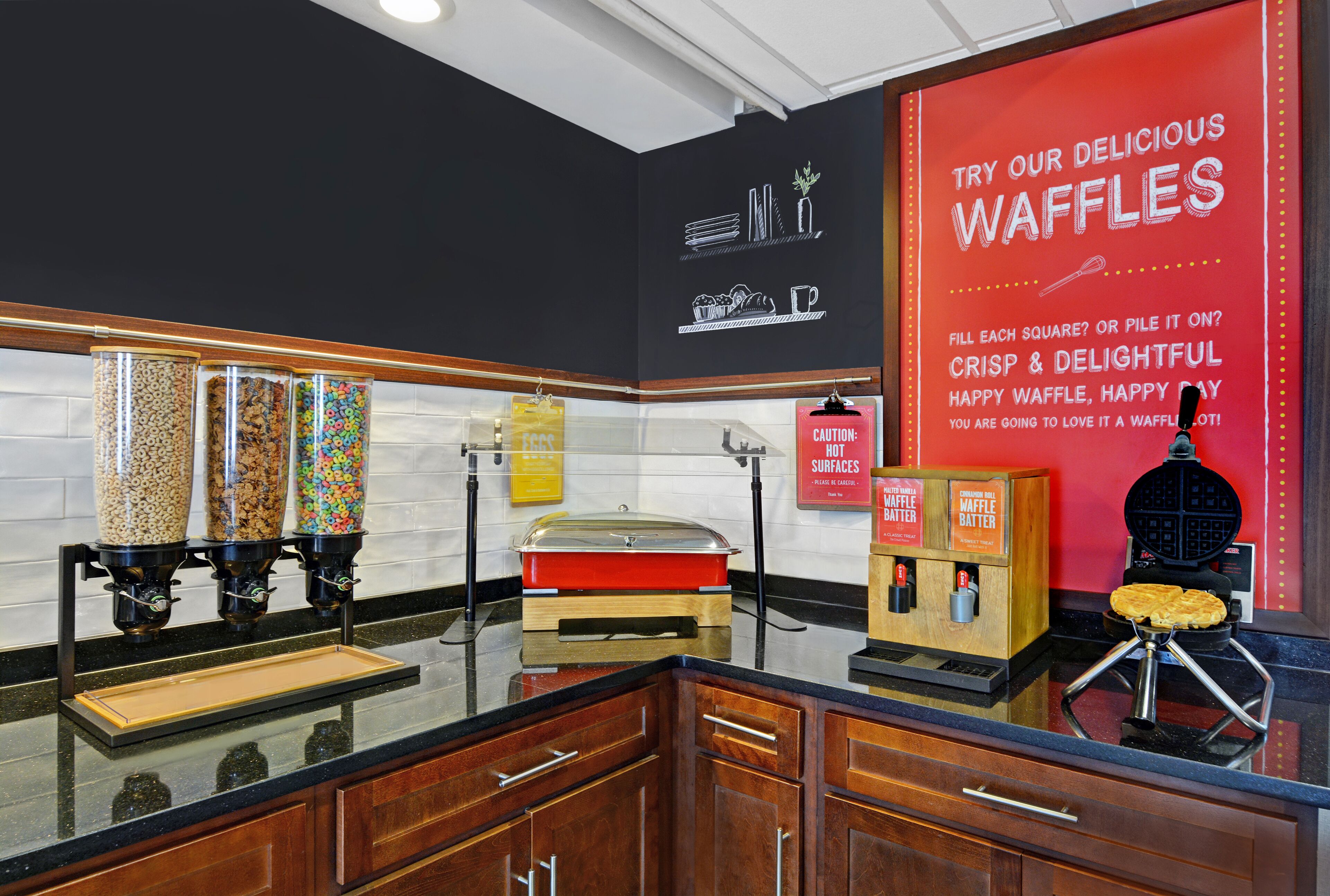 A kitchen area with waffle-making equipment, a waffle iron, and a sign promoting waffles.